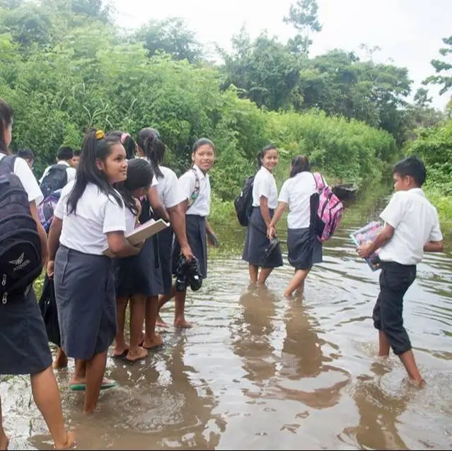Students in school uniforms wading through floodwater in El Chino, Peru
