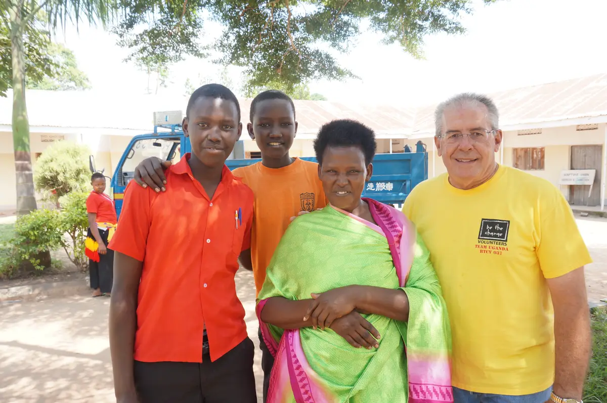 Two BTCV Kids students with a woman and a Team Uganda volunteer outside their school