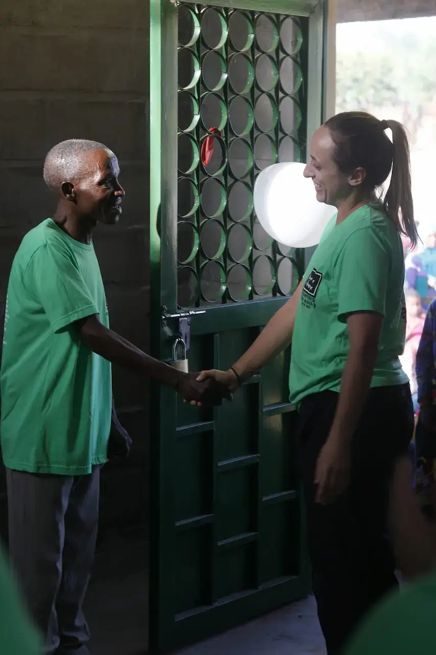 Two people in matching green shirts shaking hands in a doorway.