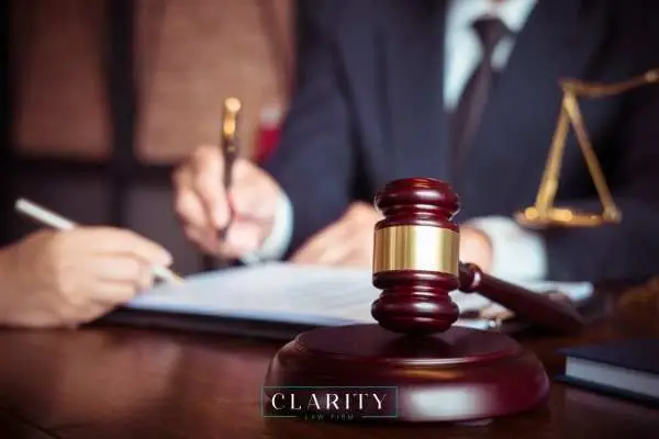 Judge’s gavel on a desk with a lawyer signing documents and a scale of justice in the background.