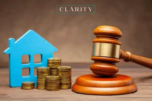 Judge’s gavel resting on a table next to stacks of coins and a blue cutout of a house