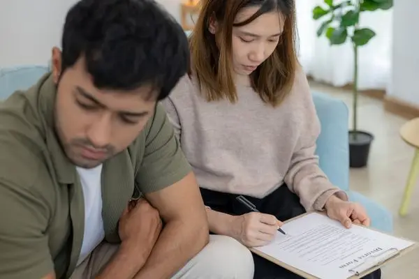 A woman signing a divorce form while a man sits beside her.