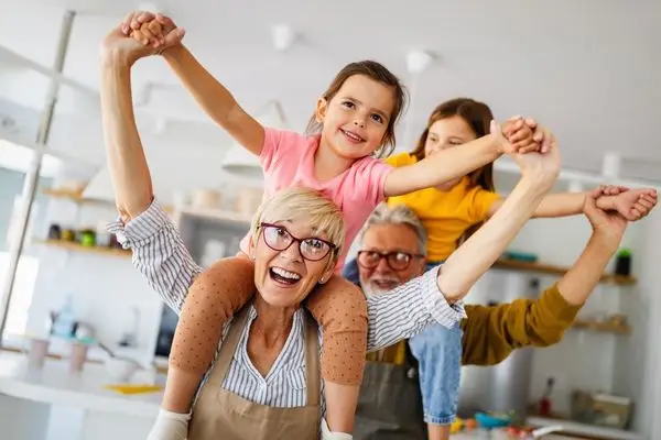A happy grandmother giving a young girl a piggyback ride, with a grandfather doing the same for another child behind