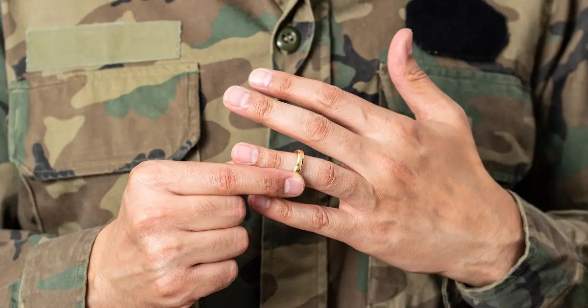 A person in military uniform removing a gold wedding ring from their finger, symbolizing a military divorce or separation.