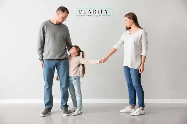 A mother and father standing apart, with their young daughter holding both their hands.