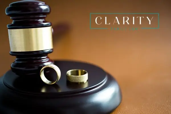 A wooden gavel rests on a brown surface next to two gold wedding rings.