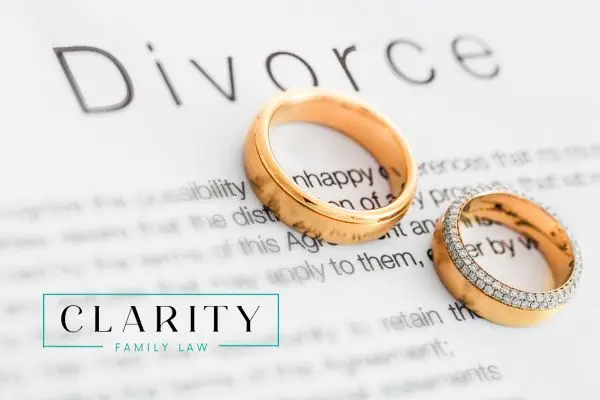 Two gold wedding rings are placed on a document that has the word 'Divorce' written on it