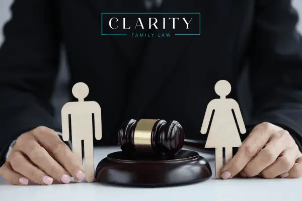 A judge's hands rest on a table, separating a wooden figure of a man and a woman with a gavel.