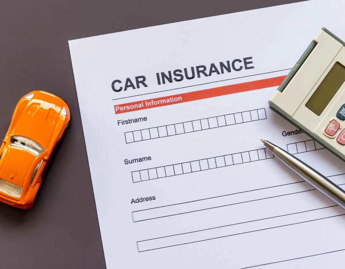 a calculator, car insurance request form, and model car on a desk