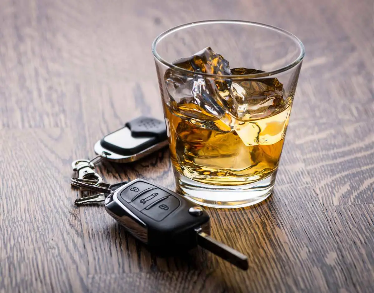 a glass of alcohol and car keys on a wooden table