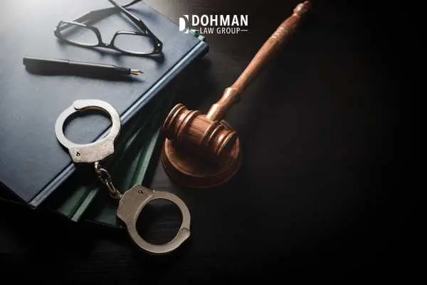 A wooden gavel, a pair of metal handcuffs, a pen, and eyeglasses resting on top of dark legal books.