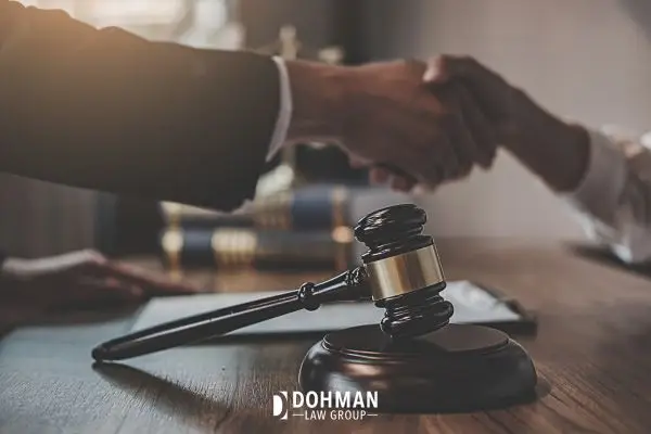 Two people shaking hands over a legal desk with a gavel.