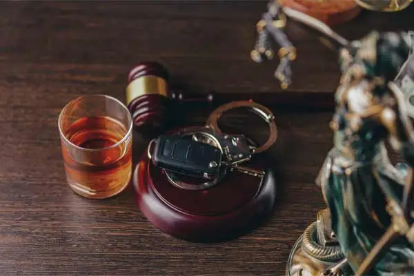 a glass of whiskey, car keys, and handcuffs next to a gavel on a wooden table