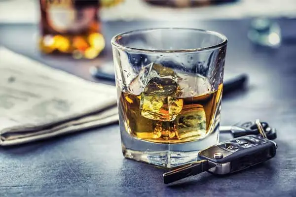 A glass of whiskey, car keys, and a newspaper on a bar.