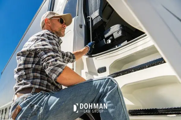 A truck driver in a plaid shirt and cap stepping into the cab of a semi-truck.