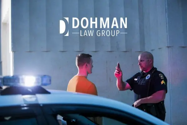 Police officer administering a field sobriety test to a driver at night with patrol car lights flashing.