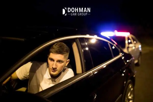 Guy in a black car looking at police lights in side mirror at night