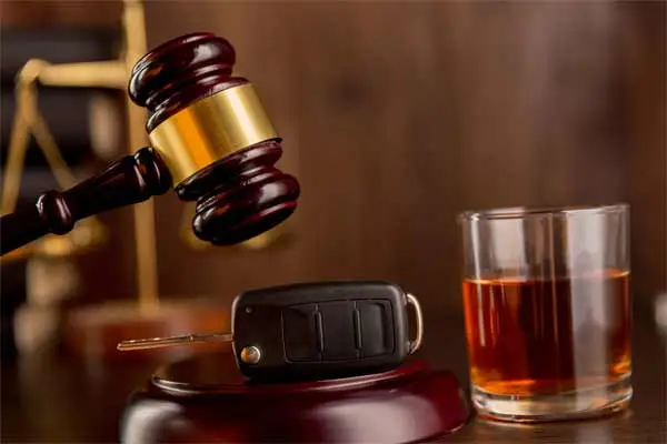 A gavel, car keys, and a glass of alcohol on a wooden surface.