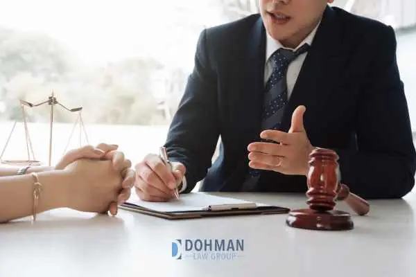A lawyer in a suit speaks with a client across a desk, with a gavel and scales of justice nearby.