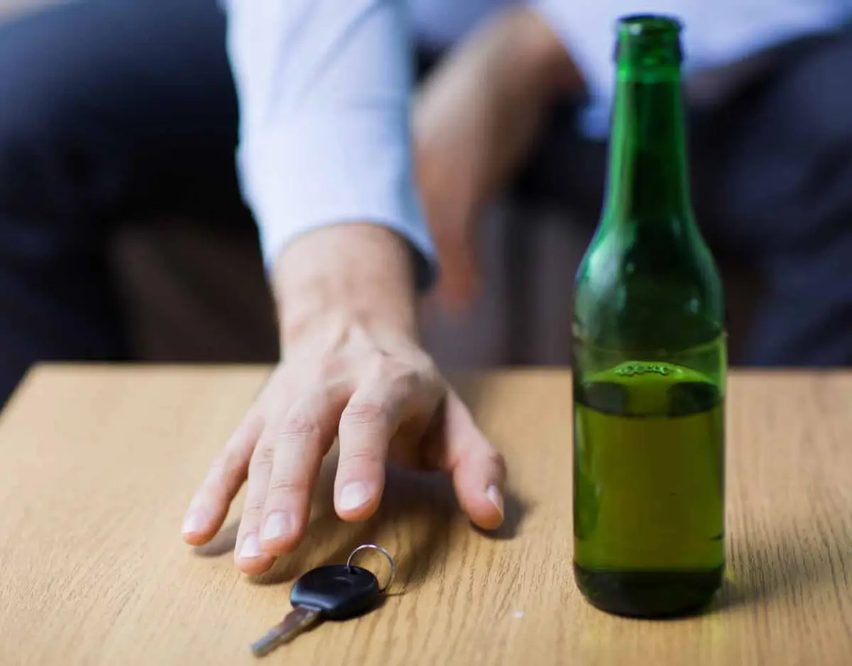 Man reaching for keys on a table beside a beer bottle