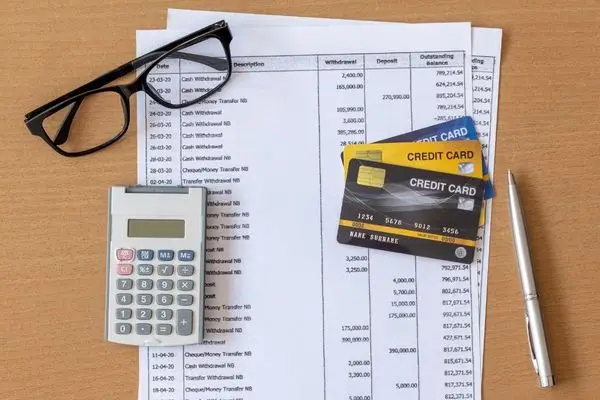 Financial documents, a calculator, and credit cards on a wooden desk.