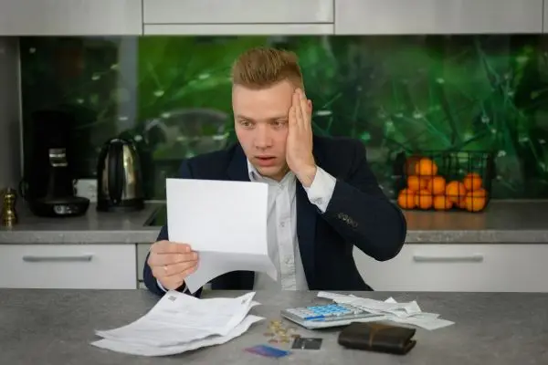 man in suit sitting in kitchen holding a letter looking worried with his credit cards out on the counter