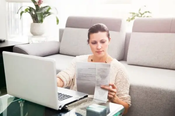 woman sitting in front of couch, checking document and using her laptop