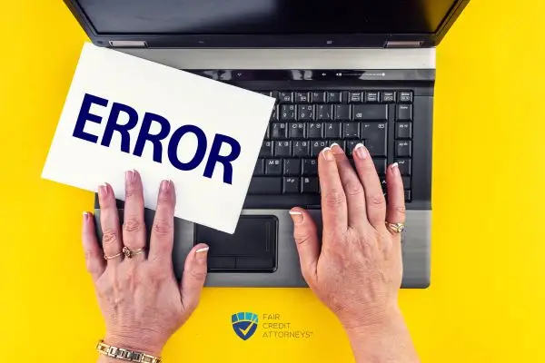 Hands on a laptop keyboard over a yellow background, with one hand holding a sign that says "ERROR".