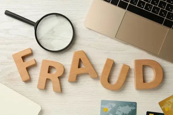 Wooden letters spelling FRAUD next to a magnifying glass and laptop.