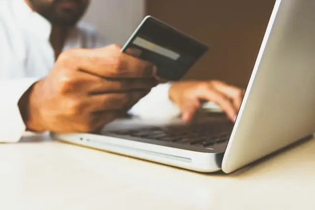 Man looks at his credit card and types on his laptop