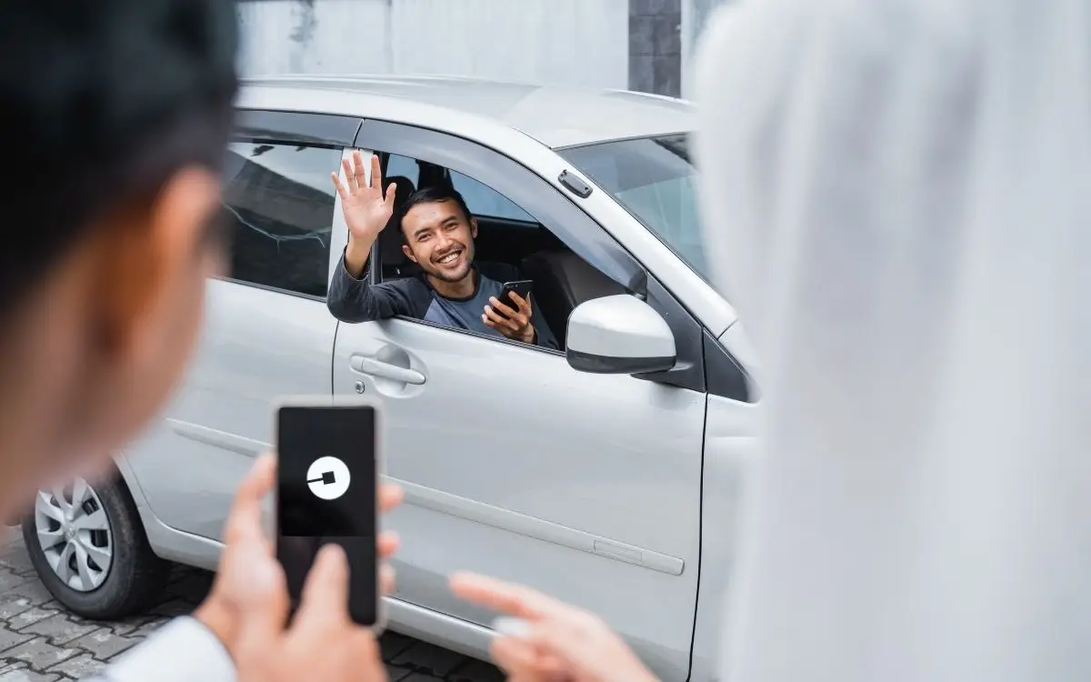 person waving from car to people looking at uber app