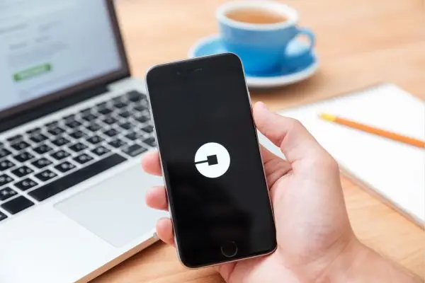 hand holding phone with Uber logo and computer in background