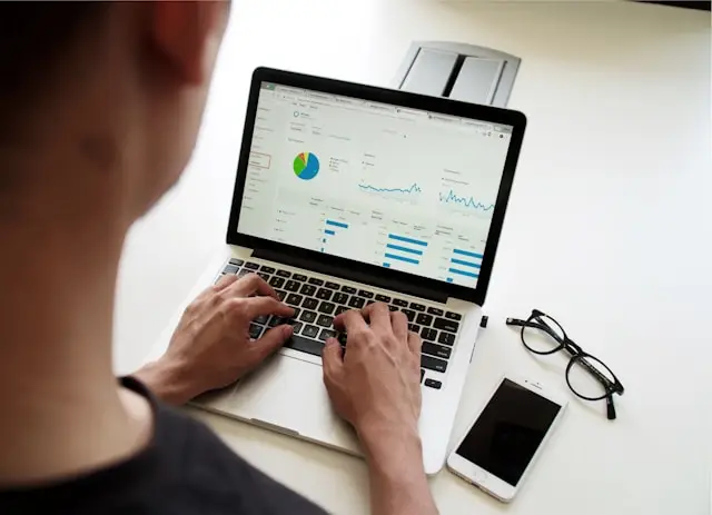 View over a man's shoulder as he works on graphs and financial documents on his computer