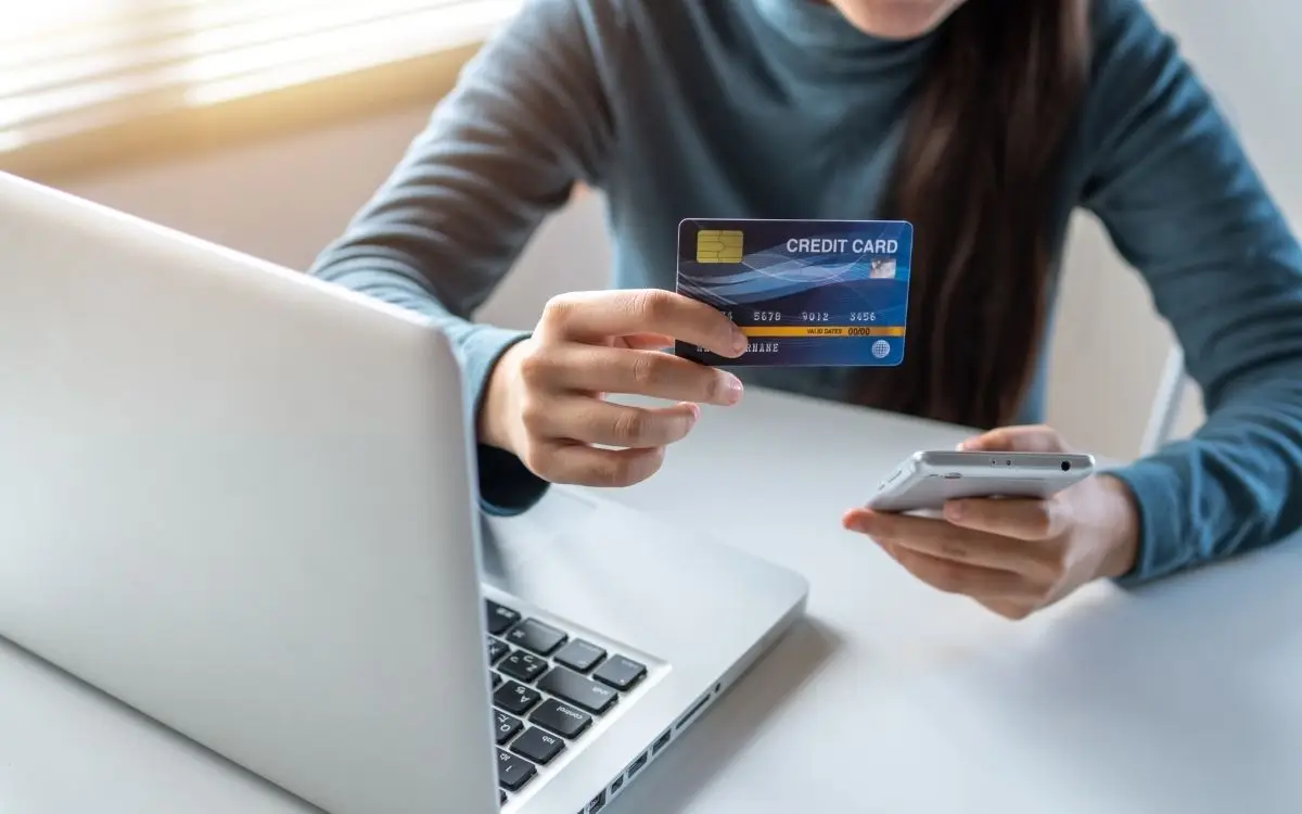 person holding credit card while on computer and holding phone