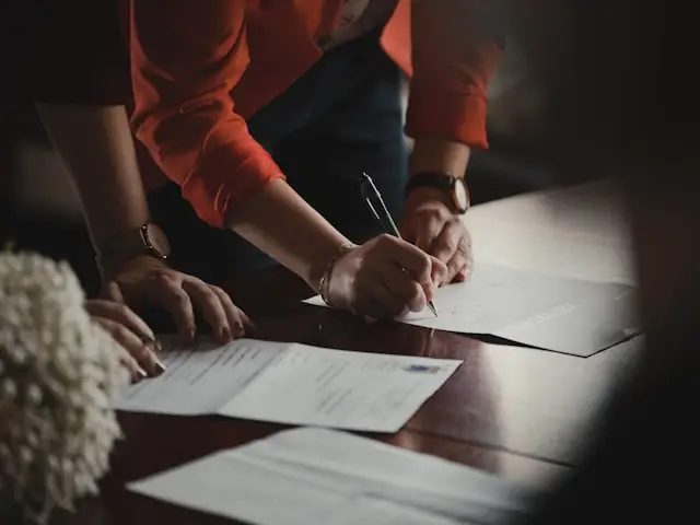 Two individuals lean over a table and one signs a document