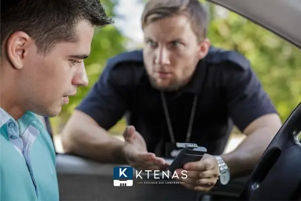 A police officer holding a breathalyzer device and looking sternly at a young driver during a traffic stop