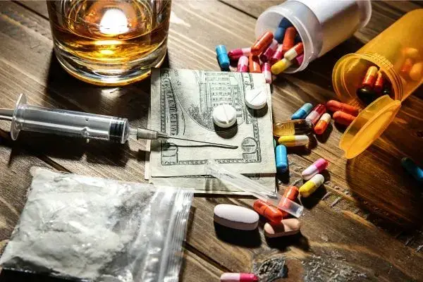 money, pills, needle, alcohol and white powder in a bag all laying on a table