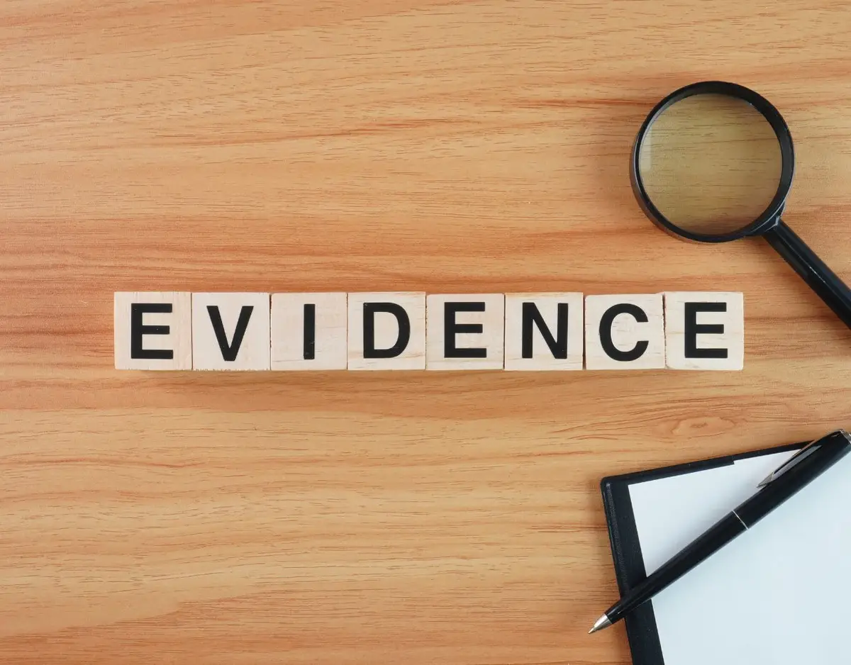 Wooden tiles spelling 'EVIDENCE' with a magnifying glass and a clipboard on a wood grain surface.