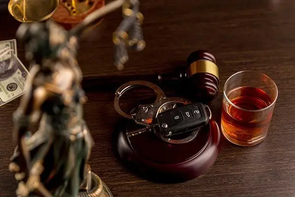 Legal symbols and car keys next to a glass of alcohol, representing a DUI