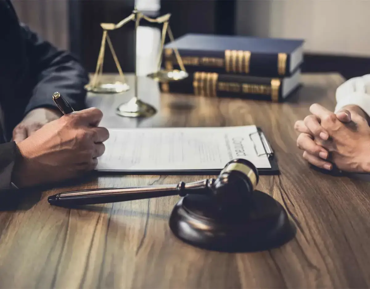 lawyer and client talking on desk with gavel, paperwork, scales, and books