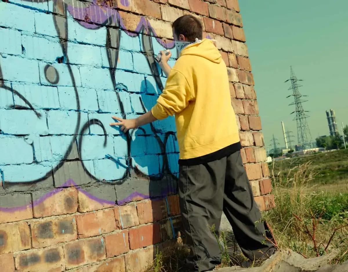 person in yellow hoodie doing graffiti
