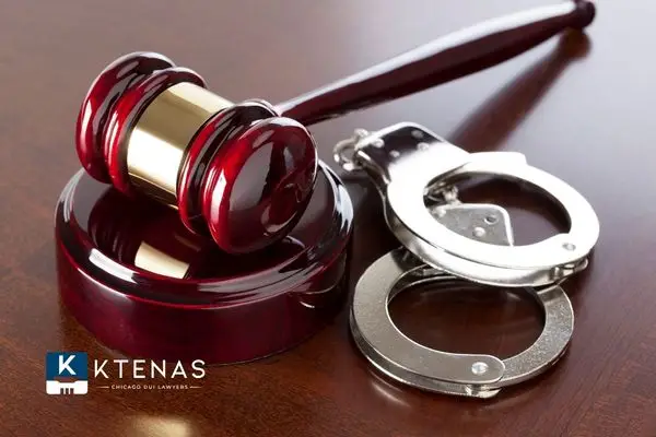 A wooden judge's gavel resting next to a pair of silver handcuffs on a wooden table.