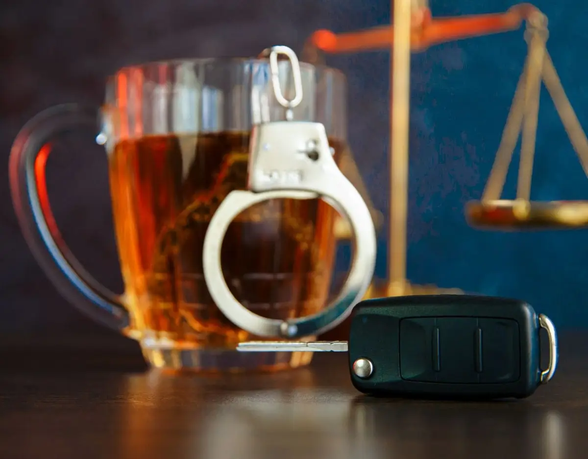 handcuffs hanging on glass of alcohol with car key in front