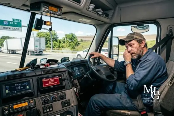 Tired truck driver rubbing his face tired with an hours-of-service violation alert on the dashboard display.
