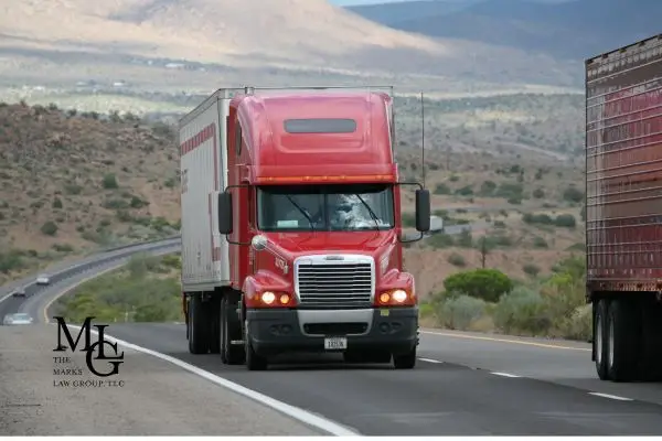 A red semi-truck driving on a winding highway through a desert landscape.