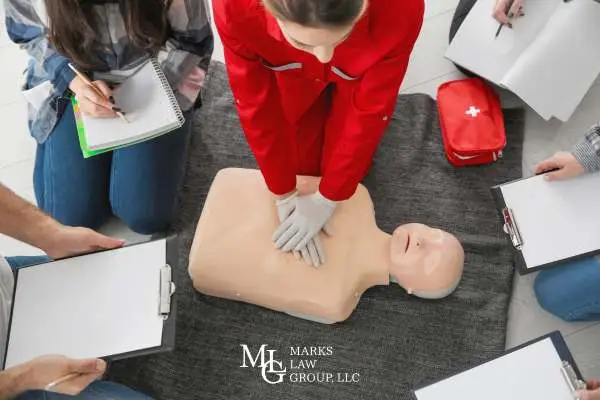 a person performing CPR on a test dummy in an educational course while attendees take notes