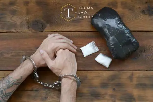 a handcuffed man sitting next to a package of drugs