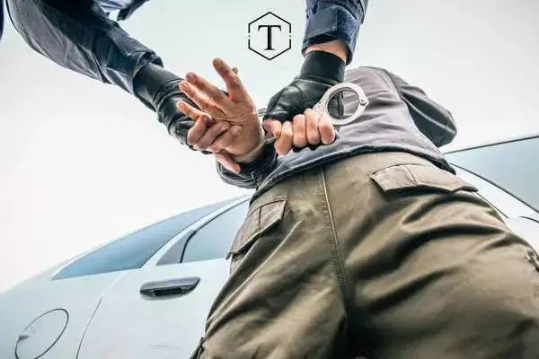 Police officer handcuffing a person against a car.