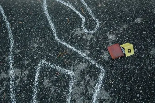Chalk outline on asphalt next to a wallet and an evidence marker block