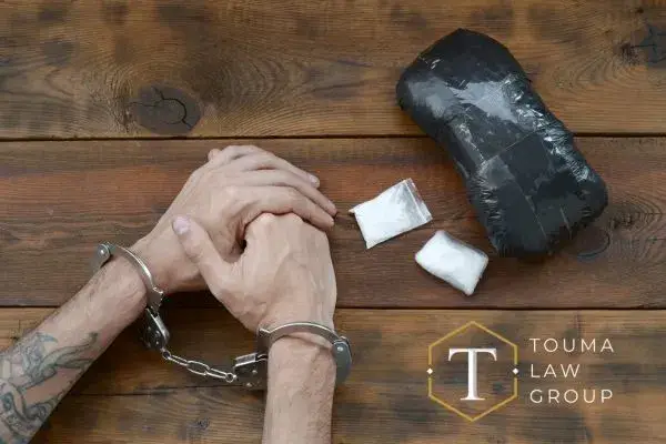 Handcuffed hands on a wooden table next to illegal drugs